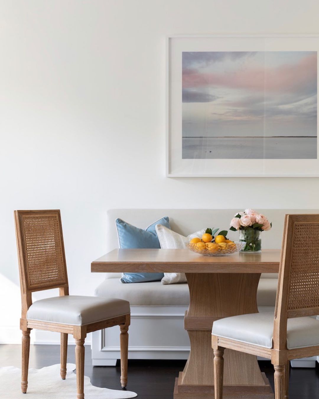 Kitchen nook with beautiful painting, bench, chairs, and table with fresh flowers and citrus